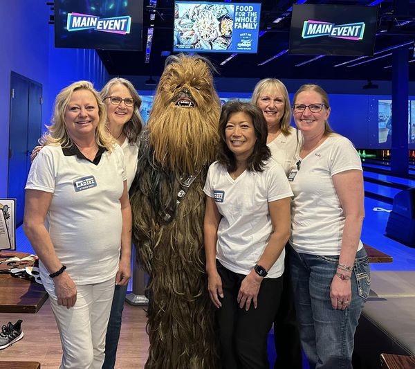 5 women standing with ChewBaca at a bowing alley after participating in a fundraiser.