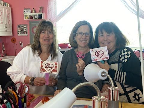 3 smiling women showing off a valentine that they had just made.