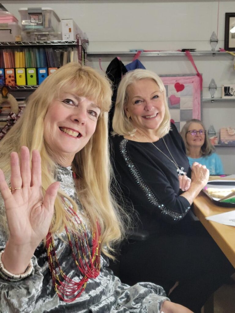 2 women smiling at the camera after working on a craft project.