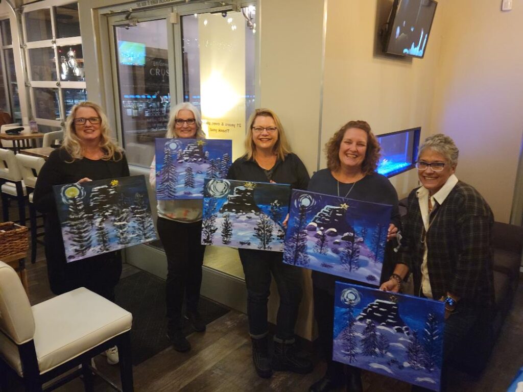 5 women holding their paintings of a snowy scene.